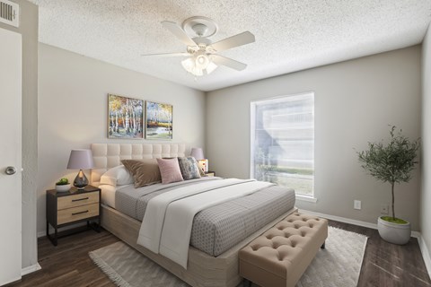 A bedroom with a large bed, a ceiling fan, and a potted plant.